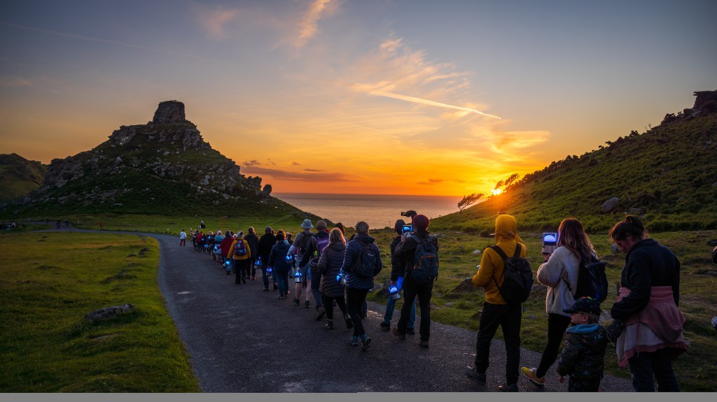 Twilight on a summer's day. A line of people with lights are walking down a path towards Castle Rock, in the Valley of Rocks, Exmoor.