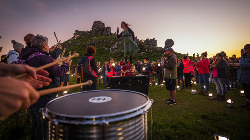 Twilight on a summers day at the Valley of Rocks, Exmoor. We see a crowd of people with lights and a clog dancer dancing on an upturned barrel. A drummer is in the foreground.